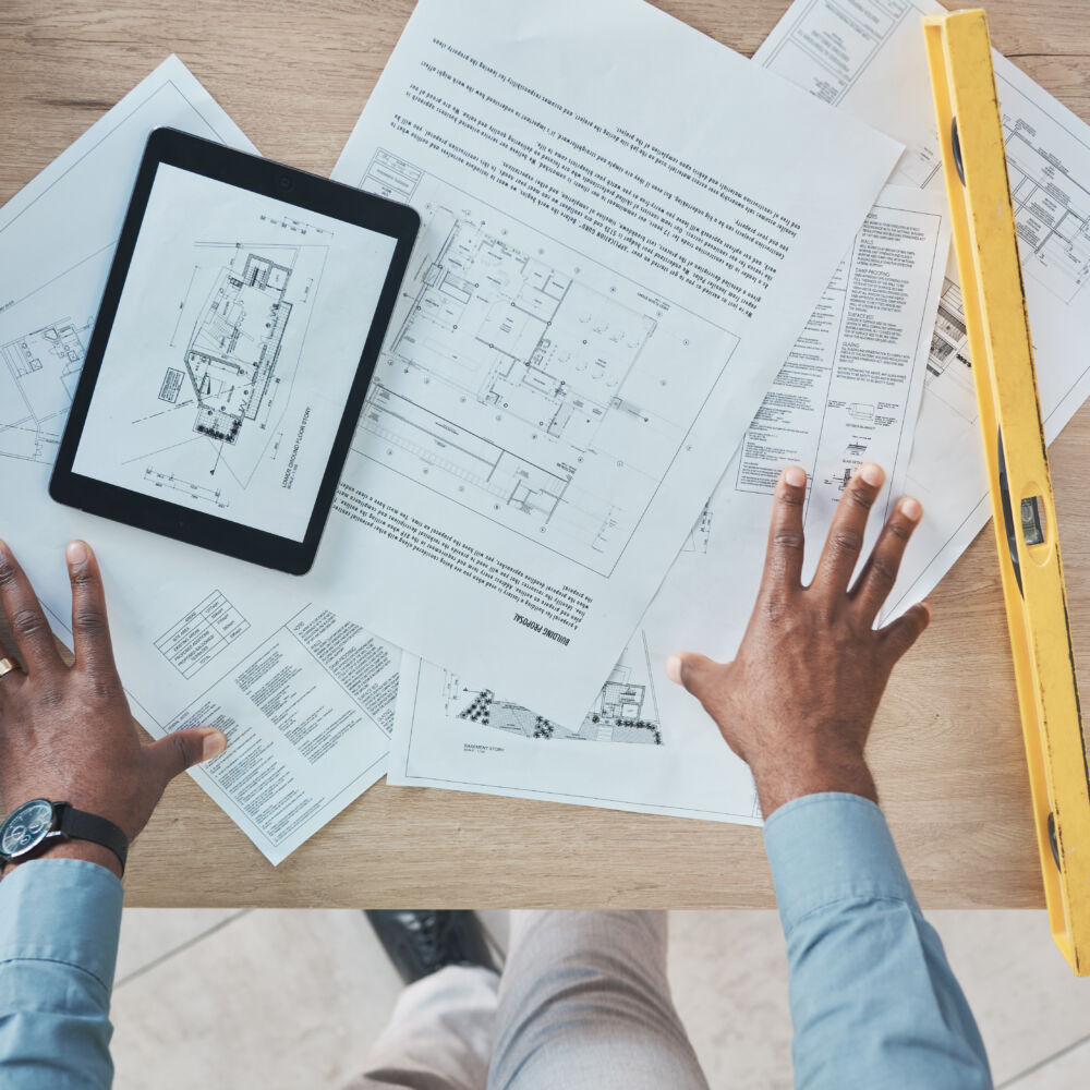 Architecture, person hands and blueprint planning, construction design and renovation on desk above. Engineering paper, floor plan and project management sketch or drawing tools on digital technology