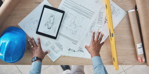 Architecture, person hands and blueprint planning, construction design and renovation on desk above. Engineering paper, floor plan and project management sketch or drawing tools on digital technology